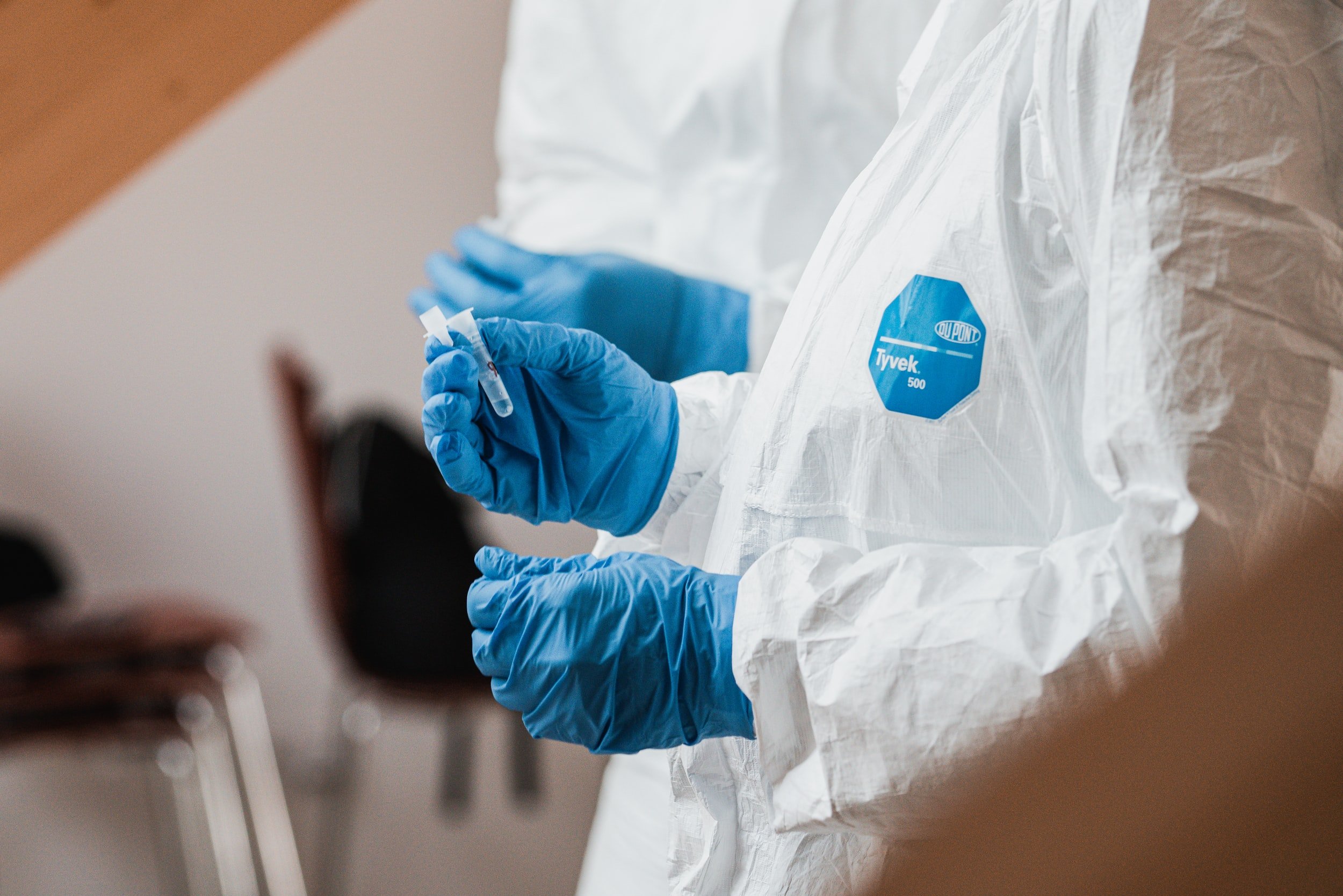 A close up of people in lab coats with blue gloves on looking at test tubes.